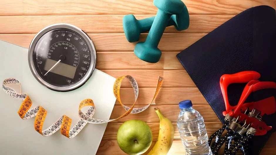 dumbbells, measuring tape, water bottle, apple, and other fitness equipment on a wooden table. SWEORN